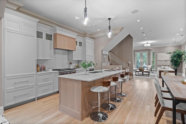 kitchen featuring a center island with sink, pendant lighting, light stone counters, light wood-type flooring, and white cabinetry