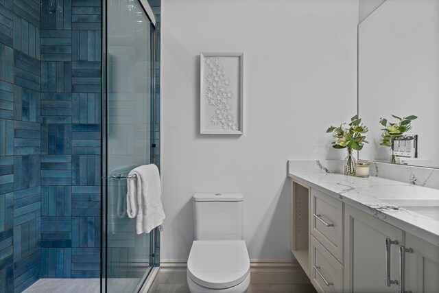 bathroom featuring a shower with shower door, double sink vanity, and toilet