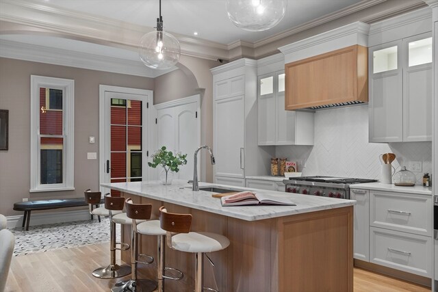 kitchen featuring white cabinetry, hanging light fixtures, decorative backsplash, an island with sink, and light hardwood / wood-style floors