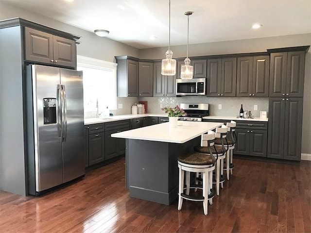 kitchen with a center island, hanging light fixtures, appliances with stainless steel finishes, dark hardwood / wood-style floors, and gray cabinets