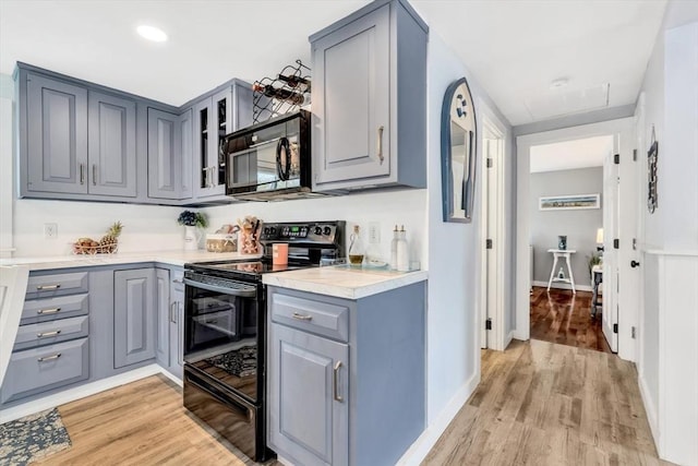kitchen featuring black appliances, gray cabinetry, light wood-type flooring, light countertops, and baseboards