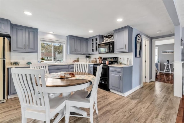 kitchen with black appliances, gray cabinets, light countertops, glass insert cabinets, and recessed lighting