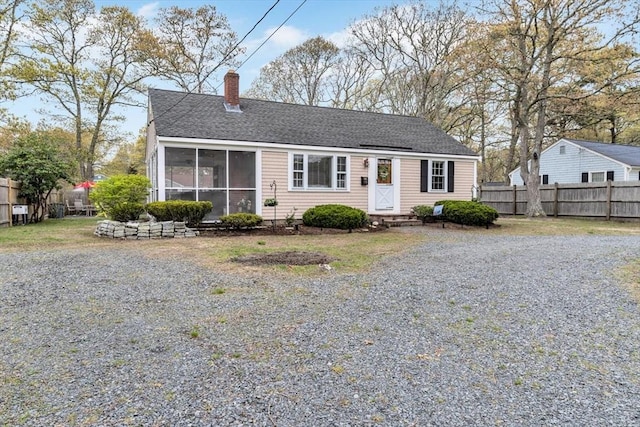 view of front of property with fence, a chimney, a sunroom, and a shingled roof