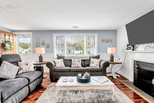 living room featuring wood finished floors, a fireplace with flush hearth, and a wainscoted wall