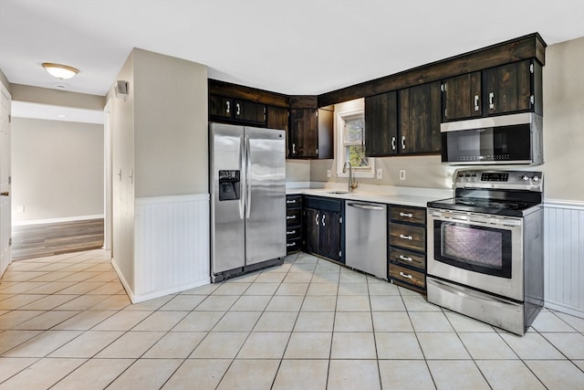 kitchen featuring stainless steel appliances, dark brown cabinets, light tile patterned floors, and sink