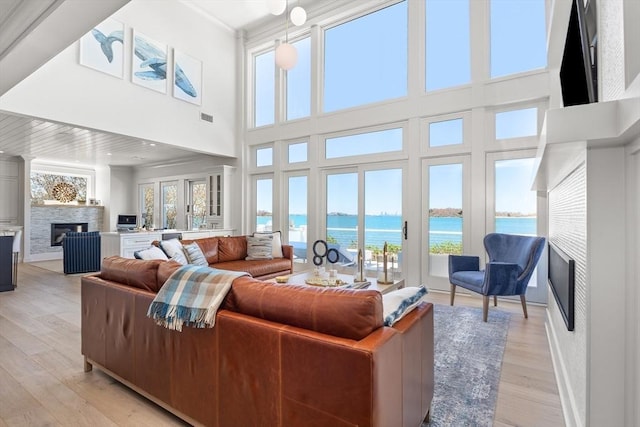 living area featuring visible vents, a fireplace, light wood-style floors, and a water view