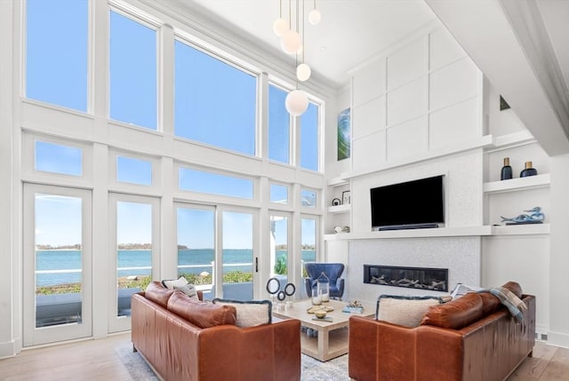 living room featuring built in shelves, wood finished floors, baseboards, a high ceiling, and a glass covered fireplace