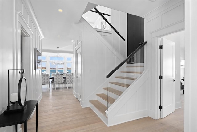 staircase with recessed lighting, a notable chandelier, wood finished floors, and a decorative wall