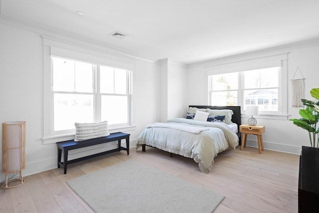 bedroom with visible vents, baseboards, light wood-style floors, and crown molding