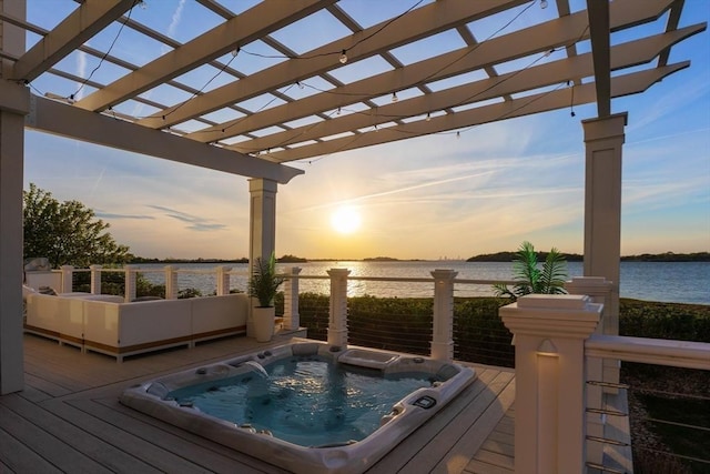 deck at dusk featuring a pergola, hot tub deck surround, and a water view