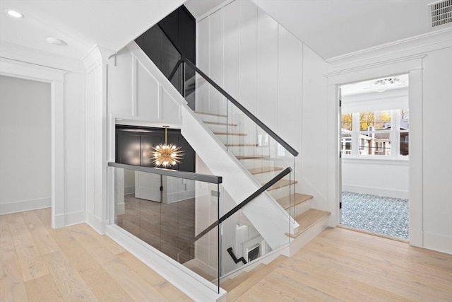 stairs with visible vents, baseboards, wood finished floors, and ornamental molding