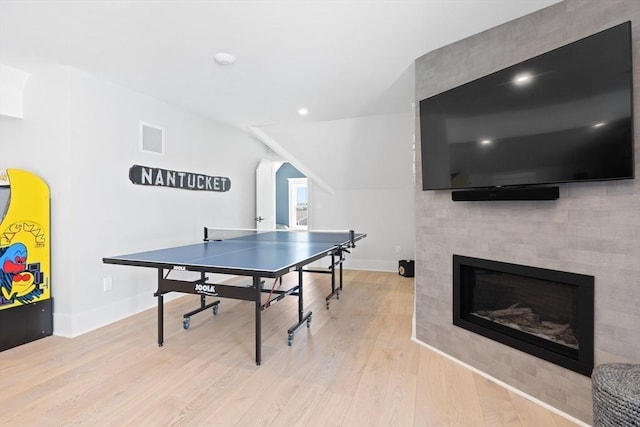 recreation room with visible vents, lofted ceiling, a glass covered fireplace, wood finished floors, and baseboards