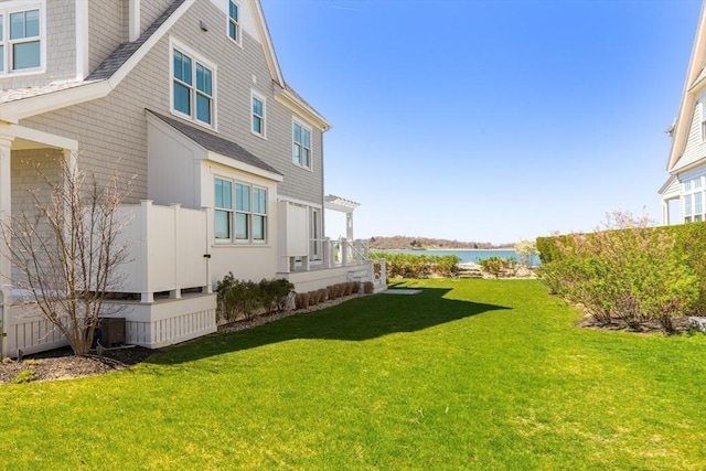 view of property exterior featuring a yard, a water view, and a shingled roof