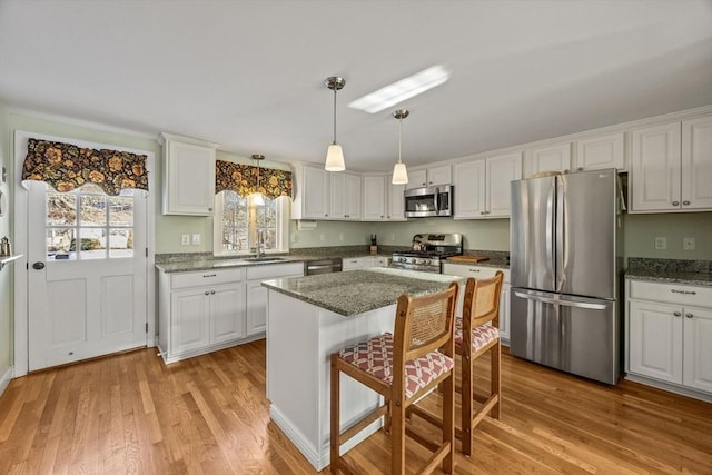 kitchen with a sink, light wood-style floors, appliances with stainless steel finishes, white cabinetry, and a kitchen bar