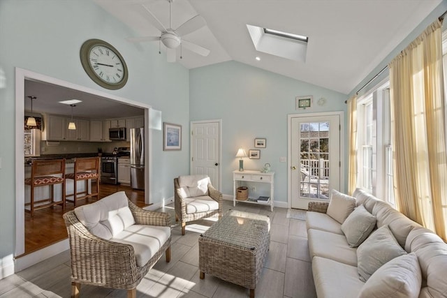 living area featuring a skylight, a ceiling fan, baseboards, and high vaulted ceiling