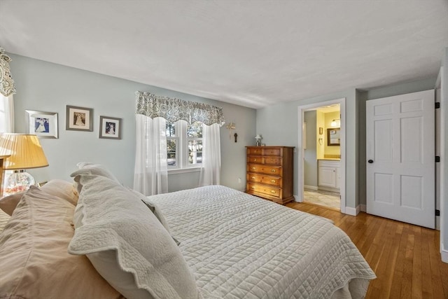 bedroom with connected bathroom, baseboards, and hardwood / wood-style floors