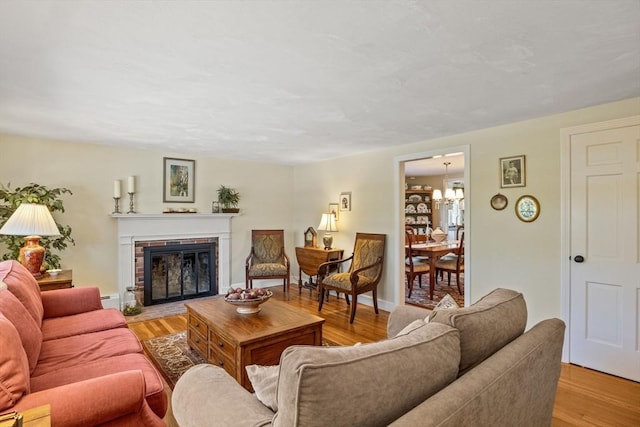 living area with a baseboard heating unit, baseboards, light wood-style floors, and a brick fireplace