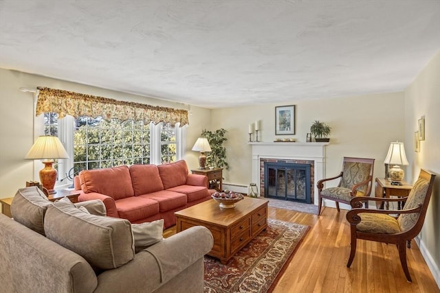 living room featuring baseboard heating, a brick fireplace, and light wood-type flooring