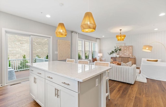 kitchen featuring white cabinetry, a center island, light stone counters, decorative light fixtures, and hardwood / wood-style flooring