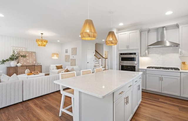 kitchen featuring appliances with stainless steel finishes, a kitchen breakfast bar, wall chimney range hood, pendant lighting, and a kitchen island