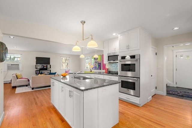 kitchen with appliances with stainless steel finishes, white cabinetry, a sink, dark stone countertops, and light wood-type flooring