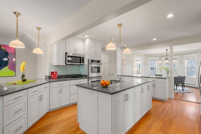 kitchen featuring light wood-type flooring, stainless steel microwave, stovetop, and a kitchen island with sink