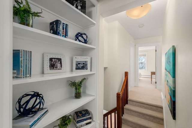 corridor with carpet floors, baseboards, built in shelves, and an upstairs landing