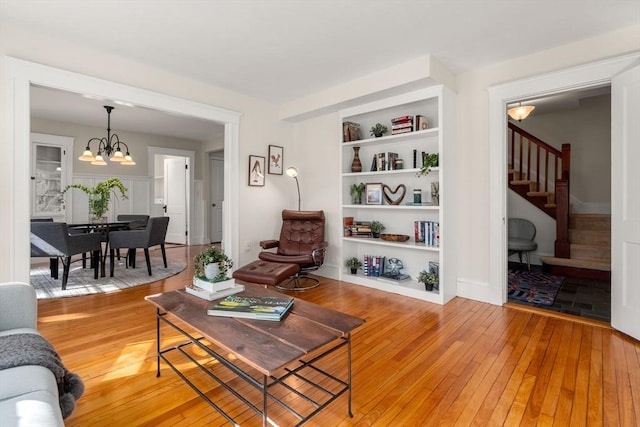 living area featuring light wood-type flooring, stairs, built in features, and a notable chandelier