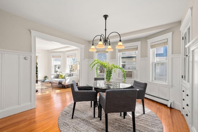 dining space with a baseboard radiator, a decorative wall, and light wood finished floors