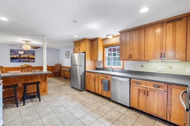 115 Winter St, Whitman, MA 02382 - kitchen with appliances with stainless steel finishes, brown cabinetry, dark countertops, a kitchen bar, and ceiling fan