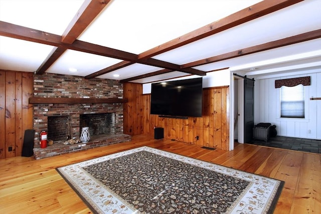 living room featuring hardwood / wood-style flooring, a fireplace, wooden walls, and beamed ceiling