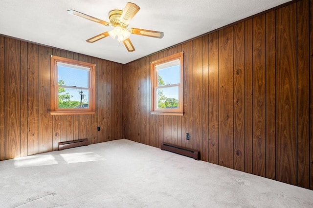 empty room featuring a baseboard radiator, carpet flooring, wooden walls, and ceiling fan