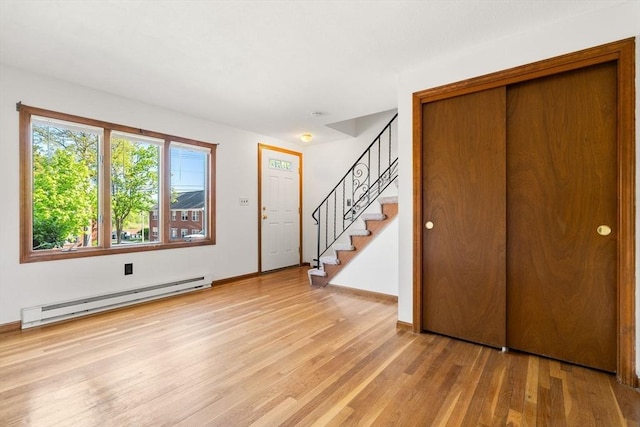 foyer featuring a baseboard radiator, light wood finished floors, stairway, and baseboards