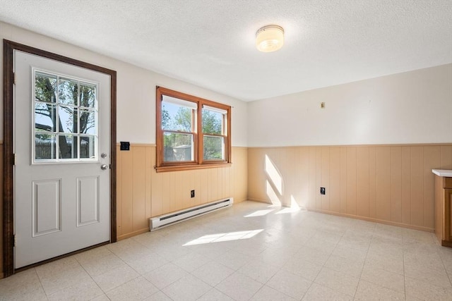 empty room with a baseboard radiator, a wainscoted wall, a textured ceiling, light floors, and baseboards