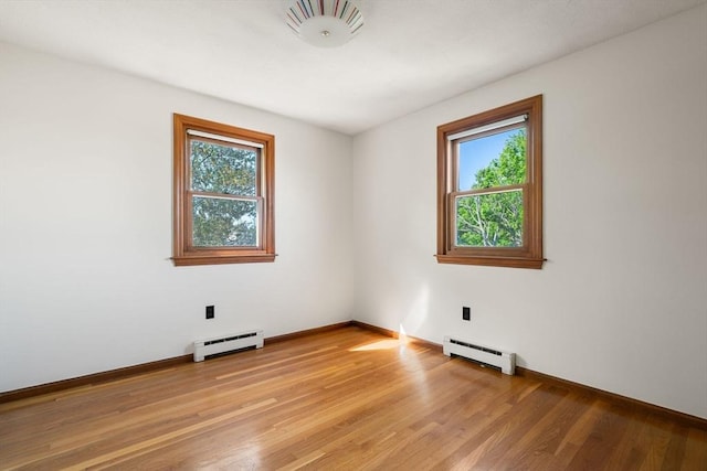 unfurnished room with a baseboard heating unit, light wood-style floors, and baseboards