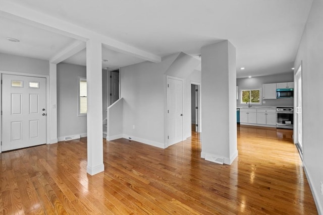unfurnished living room with light wood-style flooring, a sink, baseboards, recessed lighting, and stairway