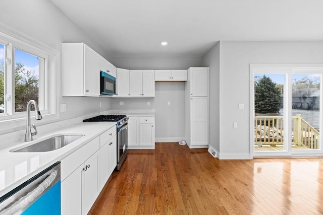 kitchen featuring stainless steel appliances, a sink, wood finished floors, light countertops, and recessed lighting