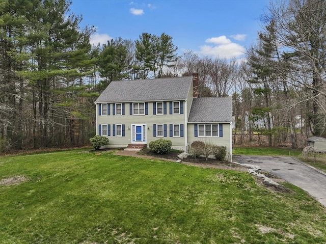 colonial home with roof with shingles, a chimney, driveway, and a front yard