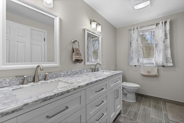 bathroom with a sink, baseboards, toilet, and double vanity