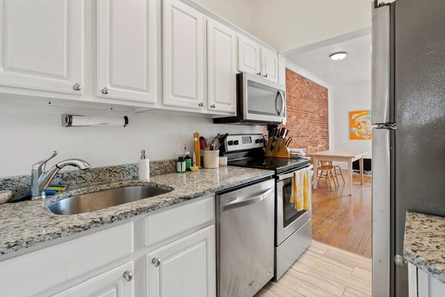 kitchen featuring a sink, stainless steel appliances, light wood-style flooring, white cabinetry, and light stone countertops