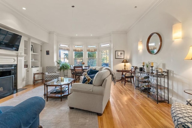 living room with a tiled fireplace, light wood-style flooring, ornamental molding, and built in shelves