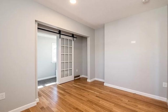 spare room with light wood finished floors, baseboards, a barn door, and recessed lighting