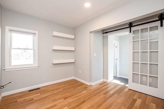 unfurnished bedroom featuring a barn door, light wood finished floors, and baseboards