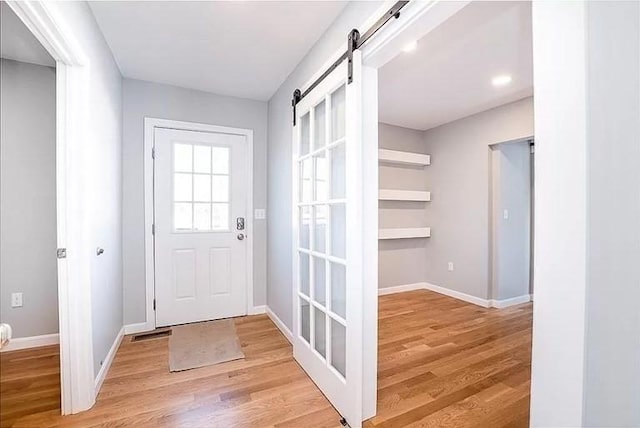 doorway with light wood-type flooring, a barn door, and baseboards