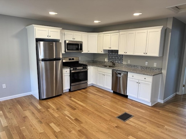 kitchen with appliances with stainless steel finishes, a sink, white cabinetry, stone counters, and recessed lighting