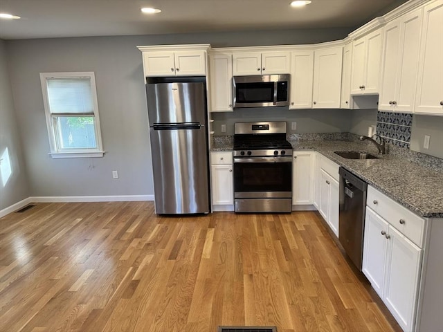 kitchen featuring stainless steel appliances, a sink, white cabinets, recessed lighting, and dark stone counters