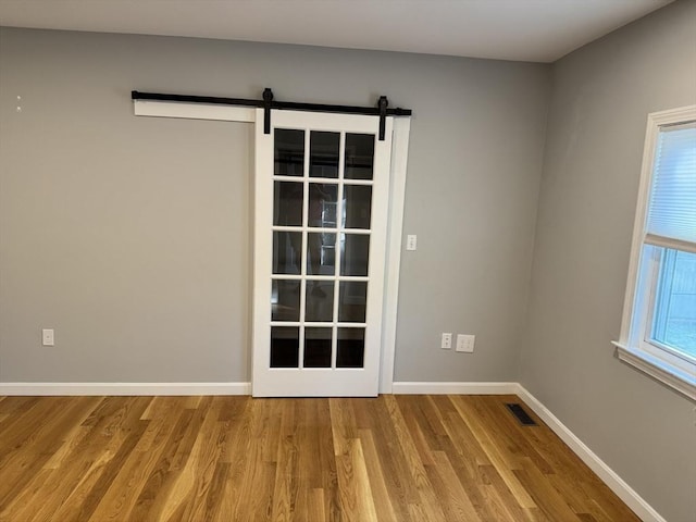 empty room with wood finished floors, a barn door, and baseboards