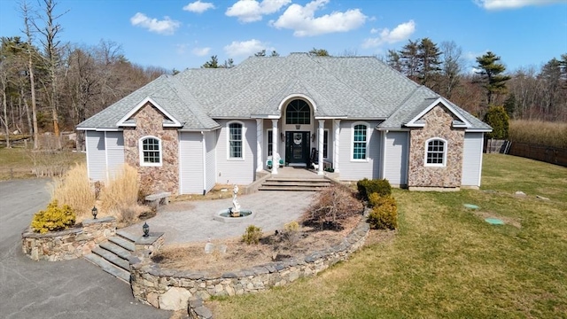 single story home with stone siding, a front yard, and roof with shingles