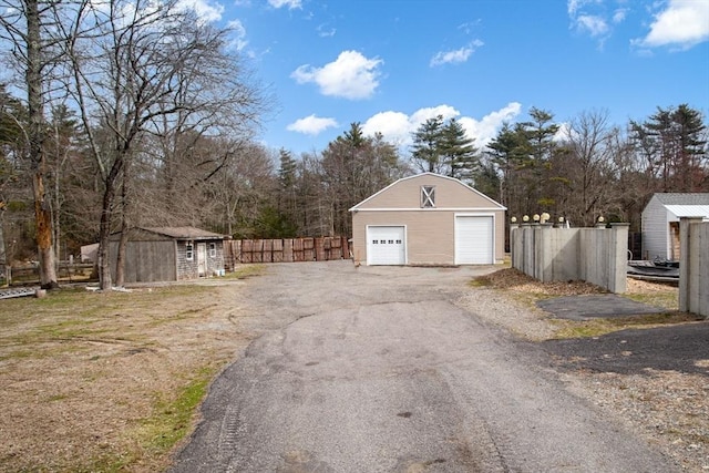 detached garage with fence, a storage shed, and view of scattered trees