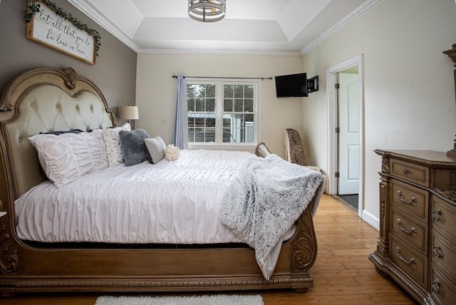 bedroom featuring a tray ceiling, light wood-style flooring, crown molding, and baseboards
